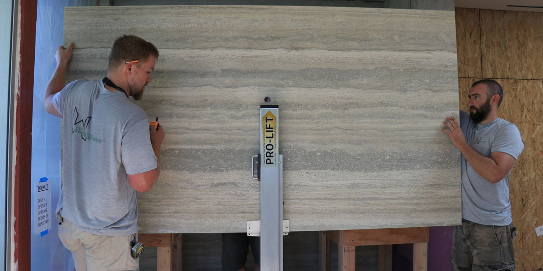 Two installers use Omni Cubed stone handling equipment to safely lift and position a large stone slab during a controlled stone installation process.